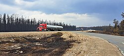 Vehicles driving out of NWT; forests on left side of road had burnt down