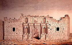 The front of a brick building; the top of the building appears torn off. Around the arched doorway are four niches, now empty. There are two small square windows.