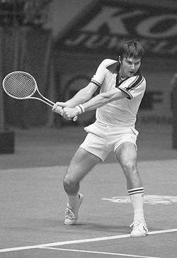 A man wearing white clothes swinging a tennis racket