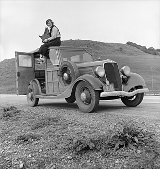 Lange in 1936 holding a Graflex 4×5 camera atop a Ford Model 40 in California, photographed by her assistant Rondal Partridge