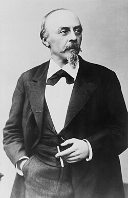  A balding man with a pointed beard, in formal dress clothes and holding a cigar in his left hand