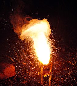 A thermite reaction using iron(III) oxide. The sparks flying outwards are globules of molten iron trailing smoke in their wake.