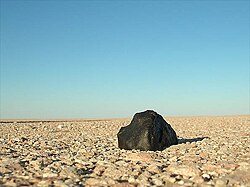 Meteorite find in situ on desert pavement, Rub' al Khali, Saudi Arabia. Probable chondrite, weight 408.5 grams (0.901 lb; 14.41 oz).