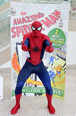 Fan dressed in Spider-Man costume after Ditko's design, posing in front of enlarged image of The Amazing Spider-Man #1 with Ditko cover art
