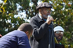 Baraka addressing the Malcolm X Festival from the Black Dot Stage in San Antonio Park, Oakland, California, while performing with Marcel Diallo and his Electric Church Band