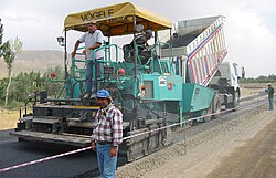 A machine laying asphalt concrete, fed from a dump truck