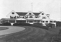 A large white house with three large gables and a porch running for much of its width stands before an expansive lawn and curved drive.