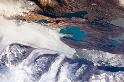 Two small icebergs at right clearly retain fragments of the moraine (rock debris) that forms a dark line along the upper surface of the glacier. The inclusion of the moraine illustrates how land-based rocks and sediment are carried by ice.