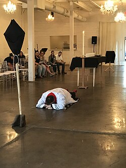 A United Methodist minister prostrates at the start of the Good Friday liturgy at Holy Family Church, in accordance with the rubrics in the Book of Worship. The processional cross is veiled in black, the liturgical colour associated with Good Friday in Methodist Churches.