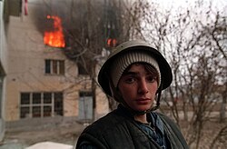 A Chechen standing near a burning house in Grozny