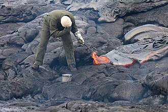A volcanologist sampling lava using a rock hammer and a bucket of water