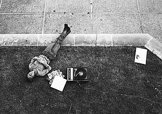 An American university student listening to a British rock record on campus while sporting newly popularized blue jeans, 1970