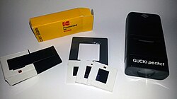 Three mini slides from 110 film, along with the box they came in from the lab, the plastic slide holder that was inside the box, a standard-format slide adapter, and a battery-powered pocket slide viewer for the mini slides