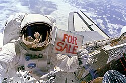 Astronaut Dale A. Gardner holding a "For Sale" sign in 1984, referring to recovered non-functional private satellites (Palapa B-2 and Westar 6, both were later successfully relaunched)