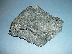 Komatiite sample collected from the Abitibi greenstone belt near Englehart, Ontario, Canada. Specimen is 9 cm wide. Bladed olivine crystals are visible, though spinifex texture is weak or absent in this sample.