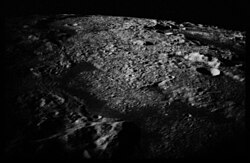 An oblique, black-and-white view of a portion of Mare Orientale from the CSM Apollo 17, illustrating the illuminating effect of Earthlight on the lunar terrain below during local nighttime; Evans reported seeing a light "flash" apparently originating from the surface in this area.