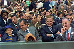 Nixon at the Washington Senators' 1969 Opening Day with team owner Bob Short (arms folded) and Baseball Commissioner Bowie Kuhn (hand on mouth). Nixon's aide, Major Jack Brennan, sits behind them in uniform