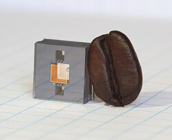 The heart of NIST's next-generation miniature atomic clock – ticking at high "optical" frequencies – is this vapor cell on a chip, shown next to a coffee bean for scale.