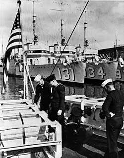American and British sailors examine depth charges. In the background are US Wickes-class destroyers before their transfer