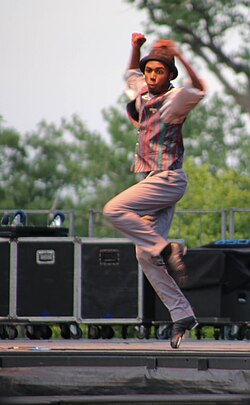 A teen tap dancer is performing a tap step known as a "toe stand" onstage.