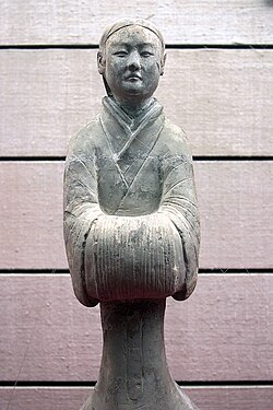 A Han dynasty (202 BC – 220 AD) Chinese ceramic figurine of a lady's maid in a standard formal pose with hands covered by long sleeve cuffs in the traditional fashion