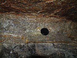 454 million-year-old volcanic ash between layers of limestone in the catacombs of Peter the Great's Naval Fortress in Estonia near Laagri. This is a remnant of one of the oldest large eruptions preserved. The diameter of the black camera lens cover is 58 mm (2.3 in).