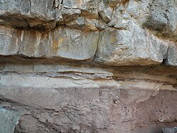 A metamorphic aureole in the Henry Mountains, Utah. The greyish rock on top is the igneous intrusion, consisting of porphyritic granodiorite from the Henry Mountains laccolith, and the pinkish rock on the bottom is the sedimentary country rock, a siltstone. In between, the metamorphosed siltstone is visible as both the dark layer (~5 cm thick) and the pale layer below it.