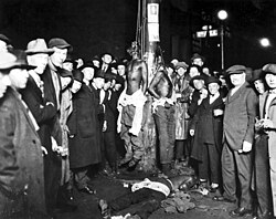 Postcard of the 1920 Duluth, Minnesota lynchings. Two of the Black victims are still hanging while the third is on the ground. Postcards of lynchings were popular souvenirs in the U.S.[101]