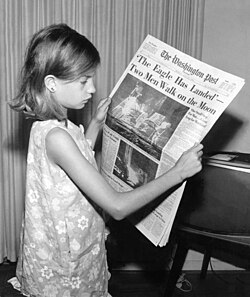 A girl reading a newspaper quoting the famous phrase 'The Eagle has landed'