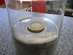 A round pound coin (density ~7.6 g/cm3) floats on mercury due to the buoyancy force upon it and appears to float higher because of the strong surface tension of the mercury.