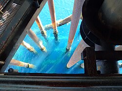 Multiple steel riser pipes extending downward through seawater below the structural deck of an offshore oil platform.