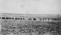 A line of men on horses charge across an open field towards the camera.