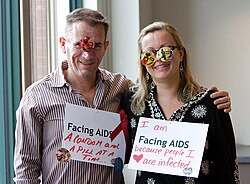 People wearing AIDS awareness signs. On the left: "Facing AIDS a condom and a pill at a time"; on the right: "I am Facing AIDS because people I ♥ are infected"