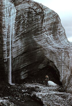 The overhanging icefront of the advancing Webber Glacier with waterfalls (Borup Fiord area, Northern Ellesmere Island) on July 20, 1978. Debris rich layers have been sheared and folded into the basal cold glacier ice. The glacier front is 6 km broad and up to 40 m high