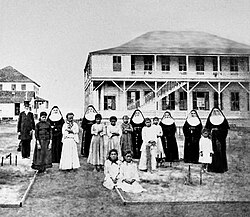 Walter Murray Gibson with the Sisters of St. Francis and daughters of Hansen's disease patients, at the Kakaʻako Branch Hospital