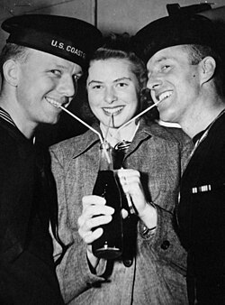 Bergman and two seamen of the United Nations—a U.S. Coast Guardsman, (left), and a Royal Navy (British) sailor—take a sip of a drink through three straws, at New York City's Stage Door Canteen that distributed cigarettes, sandwiches, coffee and other refreshments to Allied servicemen.