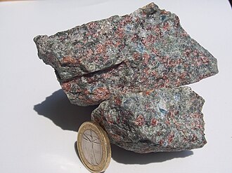Eclogite from Norway with a garnet (red) and omphacite (greyish-green) groundmass. The sky-blue crystals are kyanite. Minor white quartz is present, presumably from the recrystallization of coesite. A few gold-white phengite patches can be seen at the top. A 23 millimetres (0.91 in) coin added for scale.