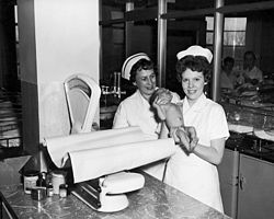 Two nurses with a baby in the nursery at Toronto East General and Orthopaedic Hospital, 1955