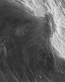 Lakshmi Planum (left) and Maxwell Montes (right) in a Magellan radar map. The highlands are covered in bright "snow," rising 5 km (3.1 mi) above the dark lava flows of the neighboring plain.[1]